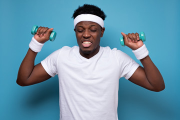 Funny african sportsman which doing exercise with lightweight dumbbells and looking at camera. It...