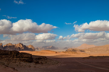 Fototapeta na wymiar Kingdom of Jordan, Wadi Rum desert, sunny winter day scenery landscape with white puffy clouds and warm colors. Lovely travel photography. Beautiful desert could be explored on safari. Colorful image