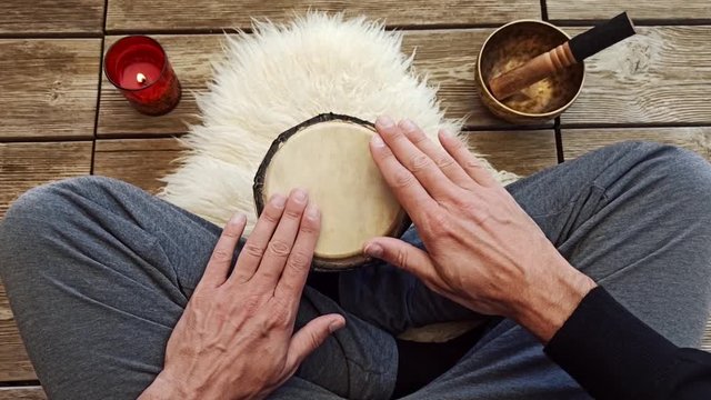 Uomo che suona un piccolo bongo seduto a gambe incrociate su background di assi di legno