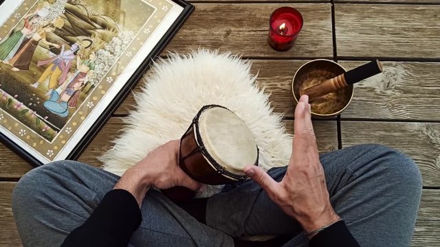 Uomo che suona un bongo seduto a gambe incrociate su background di assi di legno
