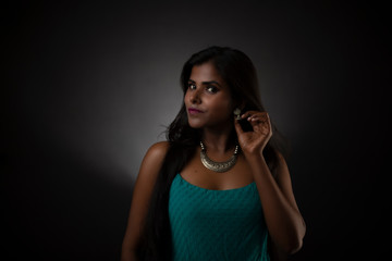 Obraz na płótnie Canvas Fashion portrait of young dark skinned Indian/African brunette girl in green western dress and jewelry in front of black copy space studio background. Indian fashion photography.