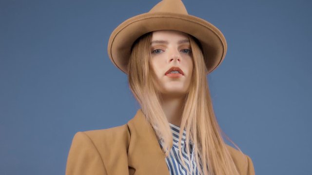 Fashion editorial portrait of blonde model touches a hat on wears an outdoor outfit
