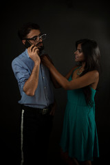 A dark skinned Indian/African girl distracting her a Kashmiri/European/Arabian husband/boyfriend while he is talking over phone in front of a black copy space studio background. Lifestyle and fashion.