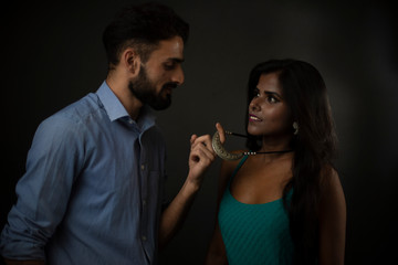 A dark skinned Indian/African girl and a Kashmiri/European/Arabian man in formal wear enjoying themselves in front of a black copy space studio background. Indian lifestyle and fashion photography.