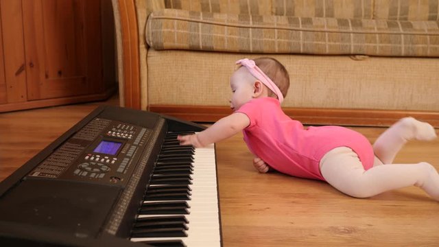 Funny baby toddler playing piano synthesizer crawling the floor at home wearing pink