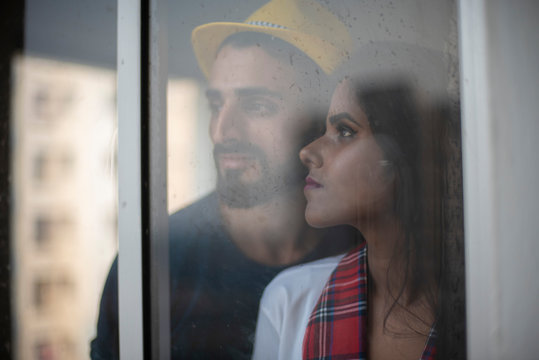 Blurred portrait of a dark skinned Indian/African girl in school uniform and a Kashmiri/European/Arabian man in casual wear and hat standing in front of closed glass window. Indian lifetsyle.