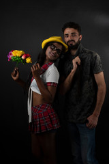 A dark skinned Indian/African girl in school uniform, hat with flowers and a Kashmiri/European/Arabian man in casual wear in front of black copy space studio background. Indian lifestyle.