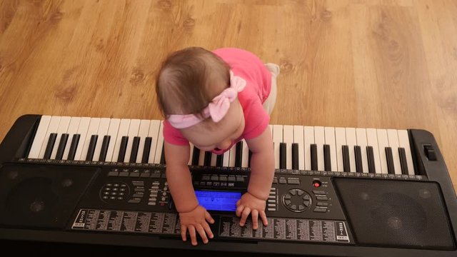 Funny baby toddler playing piano synthesizer crawling the floor at home wearing pink