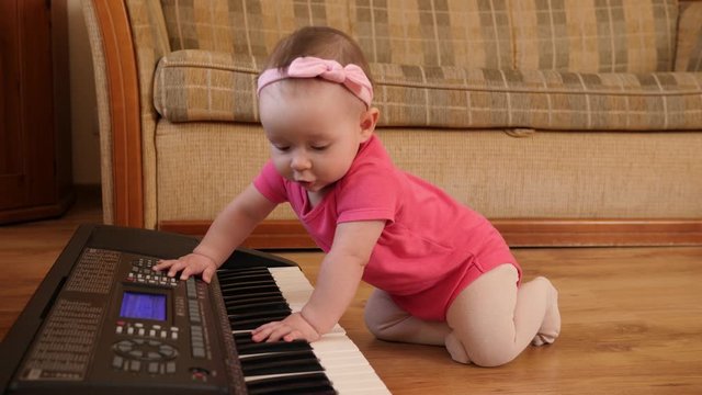 Funny baby toddler playing piano synthesizer crawling the floor at home wearing pink