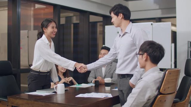 Millennial group of young businesspeople Asia businessmen and businesswomen celebrate shaking hands after dealing and signing contract or agreement at meeting room at small modern night office in city