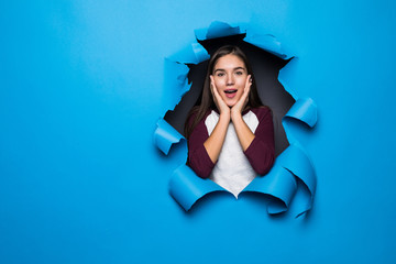 Surprised young woman looking through blue hole in paper wall.