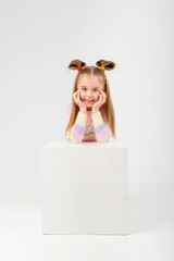 baby boy in white bodysuit stands leaning on a white cube on a light background, space for text