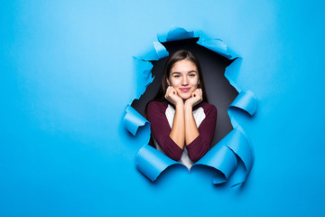 Young woman looking through blue hole in paper wall.