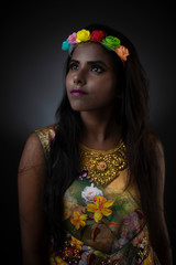 Fashion portrait of young dark skinned Indian Bengali brunette girl in floral dress with floral head band  in front of black copy space studio background. Indian fashion photography.