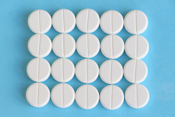 Flat lay. Group of white round pills on a blue background. Textured background. Theme of health care, medical treatment and disease prevention.