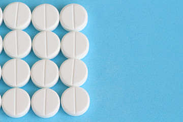 Flat lay. Group of white round pills on a blue background. Textured background. Copy space for your text. Theme of health care, medical treatment and disease prevention.