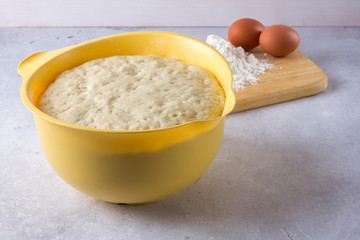 The homemade yeast dough for pizza, bread or pies is on the table in a yellow bowl.
