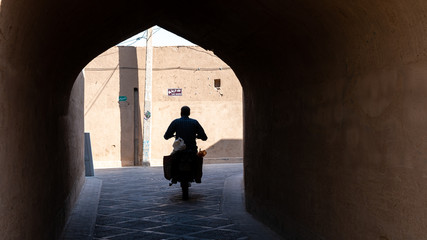 Man on a motorcycle riding in the narrow street of old city Yazd, Iran.