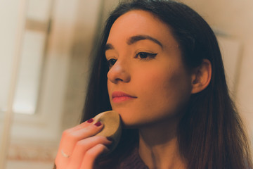 Retrato de una mujer joven y guapa maquillandose frente a une espejo