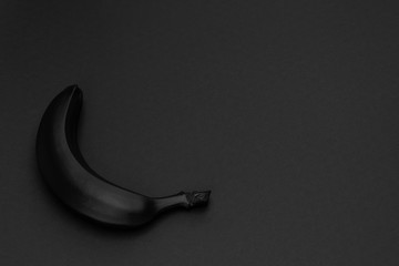 Black banana on the matte black background. Minimal style. Conceptual minimalist black art. Matte surface. Fruit. One. Space for text