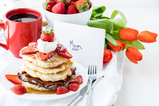 Close up of a stack of pancakes with a card, flowers and coffee for Mother's Day. A Mother's Day concept.