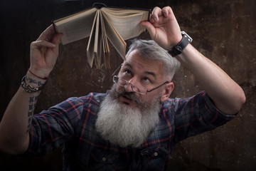 Portrait of a gray-haired bearded man with glasses turned over a book in Russian, selective focus
