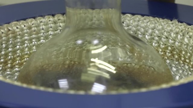 Laboratory flask with crude oil. Lab test petroleum in the background. The operation of the laboratory unit for the catalytic cracking of used oil. Oil boils in a flask.
