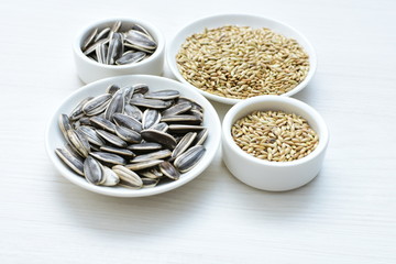 Birdseed and natural sunflower seeds, food for birds, displayed in containers on white wooden background