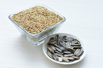 Birdseed and natural sunflower seeds, food for birds, displayed in containers on white wooden background