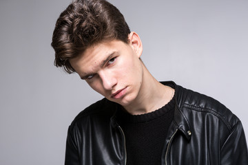 Wide angle. Studio shot. Young caucasian guy model in black clothes posing in the studio. Teenager in Leather Jacket Standing at White Background. young fashion model wearing black coat in studio