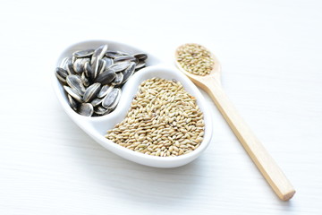 Birdseed and natural sunflower seeds, food for birds, displayed in containers on white wooden background