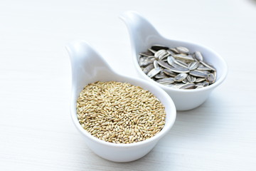 Birdseed and natural sunflower seeds, food for birds, displayed in containers on white wooden background