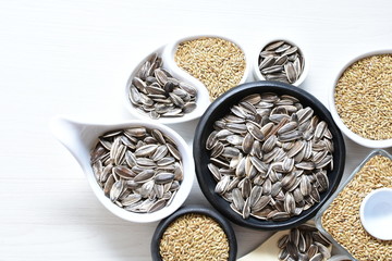 Birdseed and natural sunflower seeds, food for birds, displayed in containers on white wooden background