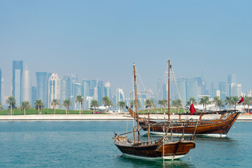 Fototapeta na wymiar Retro historical boat with blurred panoramic view of modern skyline of Doha and green palms on background
