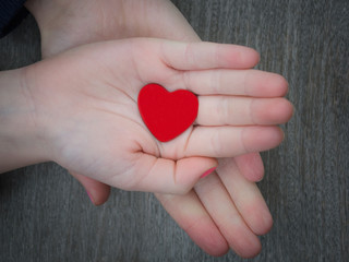 Two kids holding red heart in hand over solid wooden background in a conceptual image of love, family and care.