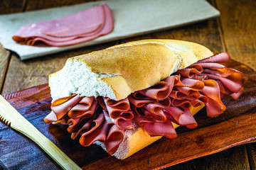 mortadella, pork slices, on italian bread, on rustic wooden background. A mortadella sandwich is...