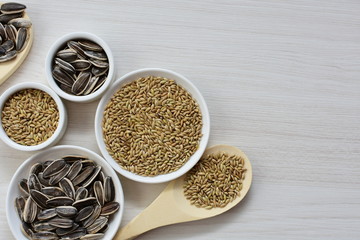 Birdseed and natural sunflower seeds, food for birds, displayed in containers on white wooden background