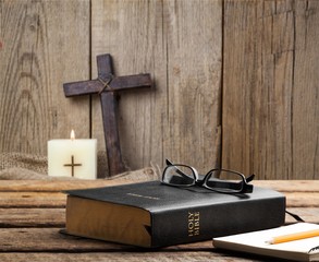 Burning candle and Bible and cross on wooden desk