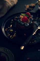 Czekoladowe babeczki z malinami i jagodami na czarnym talerzu, styl Moody, Zdjęcie żywności w ciemnych kolorach, - 329643393