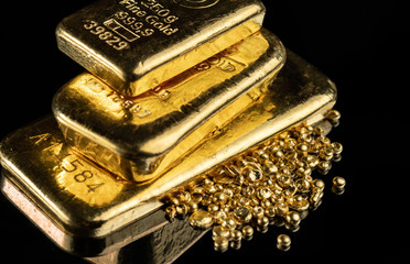 Several gold bars of different weight and a pile of pure gold granules on a mirror dark background.