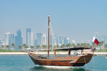 Naklejka na ściany i meble Retro historical boat with blurred panoramic view of modern skyline of Doha and green palms on background
