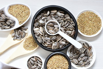 Birdseed and natural sunflower seeds, food for birds, displayed in containers on white wooden background