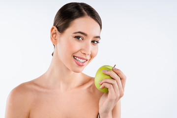 Happy attractive woman holding fresh apple and looking at it while standing against white background. Skin care concept