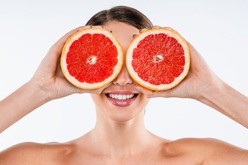 Smiling young woman posing isolated over white wall background holding grapefruit covering eyes
