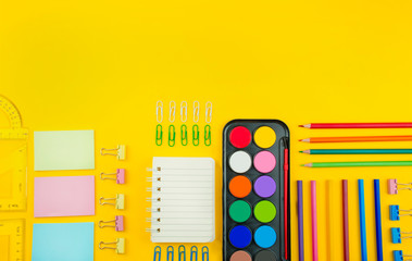 School supplies on a bright yellow background. Multicolored wooden pencils, notebook, paper clips,...