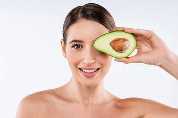 Young woman holding half an avocado in front of her face isolated on white background. Beauty & Skin care concept