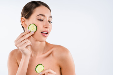 Beauty portrait of attractive woman holding sliced cucumber standing isolated over white background