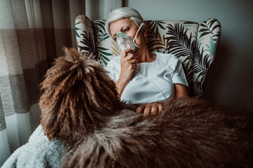 White-haired middle-aged woman with medical treatments at home. Assisted breathing to eliminate...