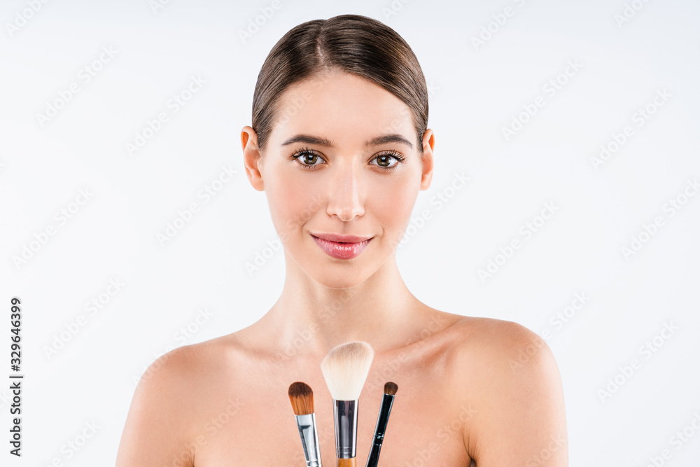 Wall mural Portrait of young woman smiling and holding make up brushes isolated on white background. Cosmetic beauty concept