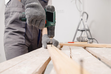 Worker man carpenter screws metal into wooden board with electric screwdriver